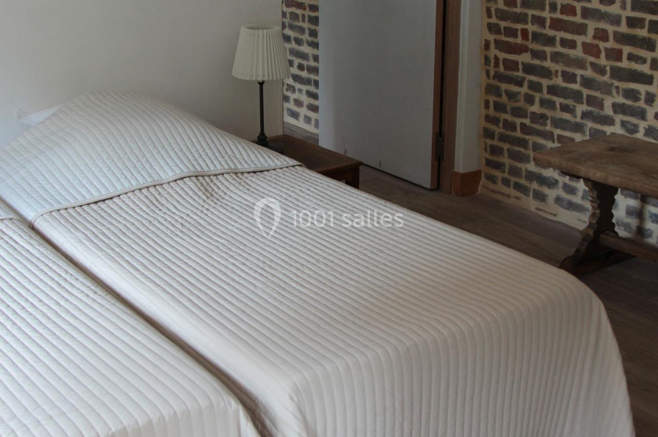 Deux lits simples rapprochés avec des couvre-lits blancs dans une chambre aux murs en briques et sol en parquet.