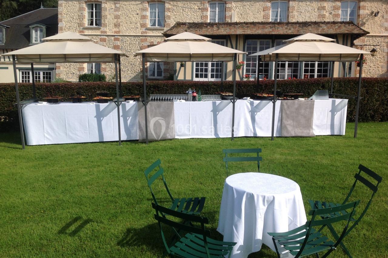 Buffet extérieur sous des parasols devant une maison en pierre, avec des tables et chaises sur une pelouse.