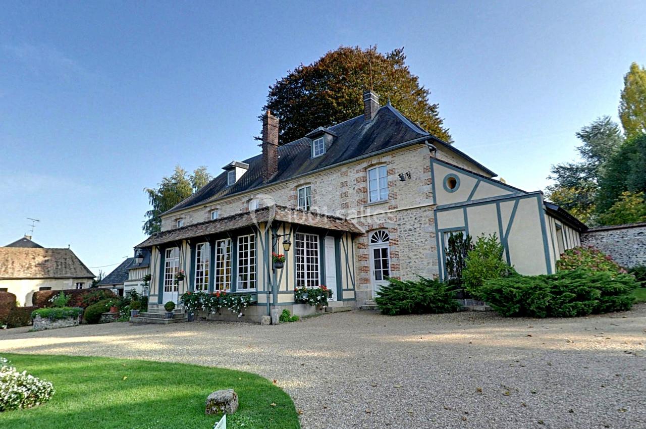 Façade d'une maison traditionnelle à colombages entourée d'un jardin avec allée gravillonnée.