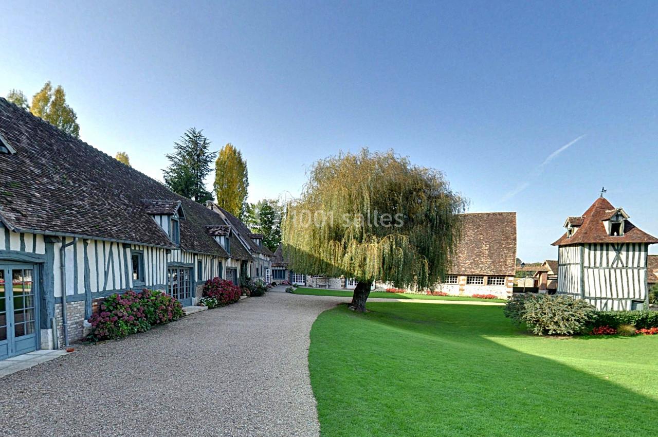Allée bordée de maisons à colombages, pelouse bien entretenue et un grand saule au centre.