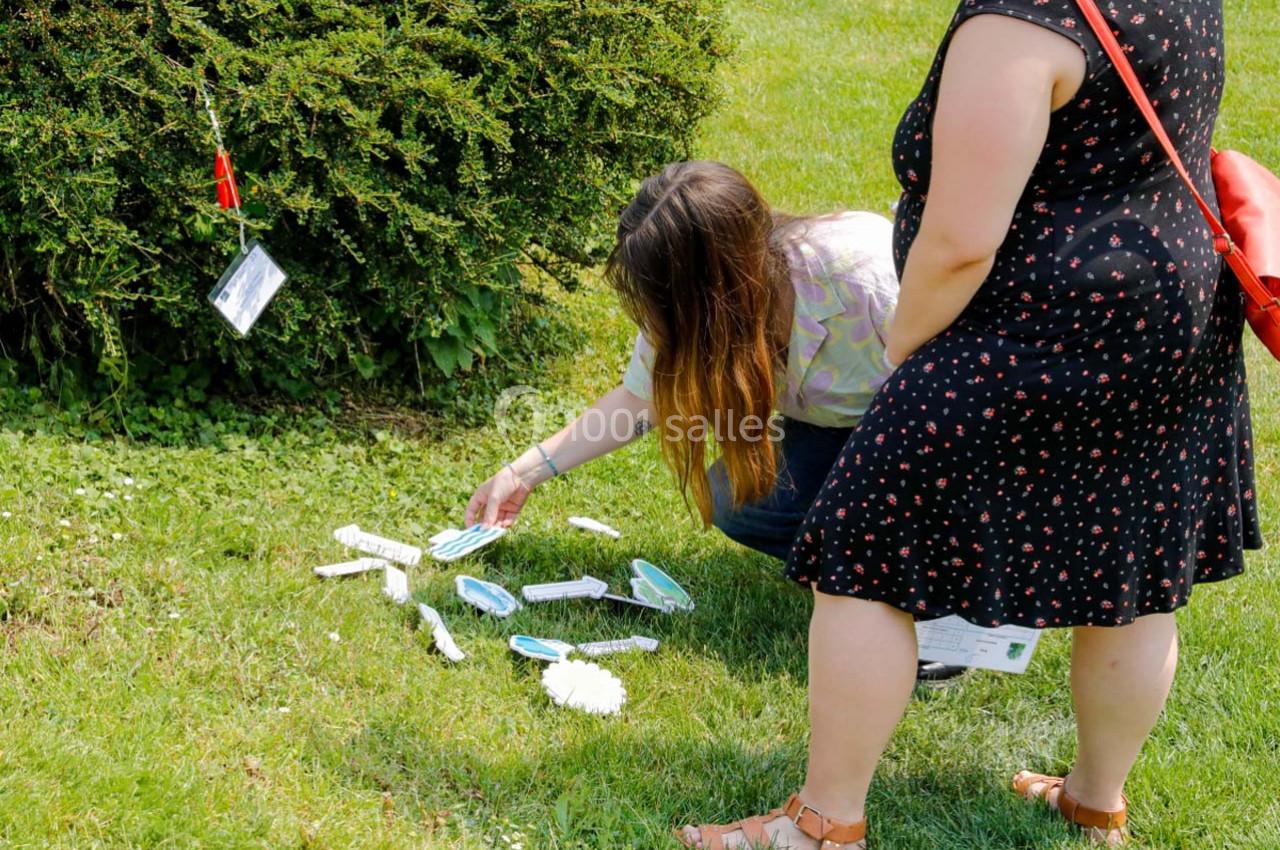 Deux personnes ramassent des objets en plastique éparpillés sur une pelouse près d'un buisson.
