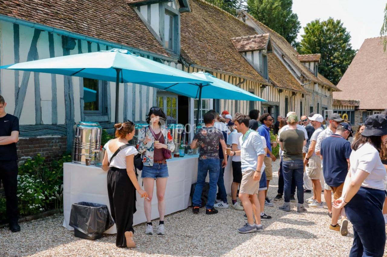 Des personnes font la queue devant un stand de boissons installé en extérieur, près de bâtiments à colombages.