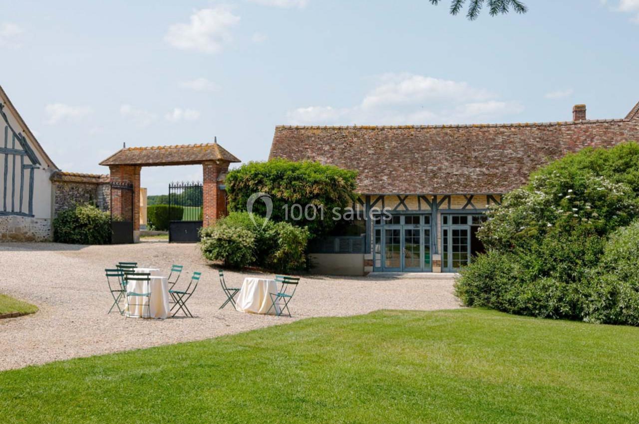 Cour extérieure avec pelouse, mobilier de jardin et bâtiments à colombages sous un ciel dégagé.