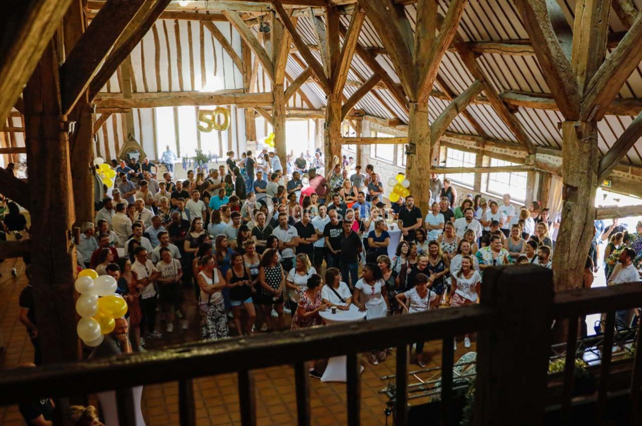 Groupe de personnes rassemblées dans une grande salle en bois avec des décorations et des ballons jaunes et blancs.