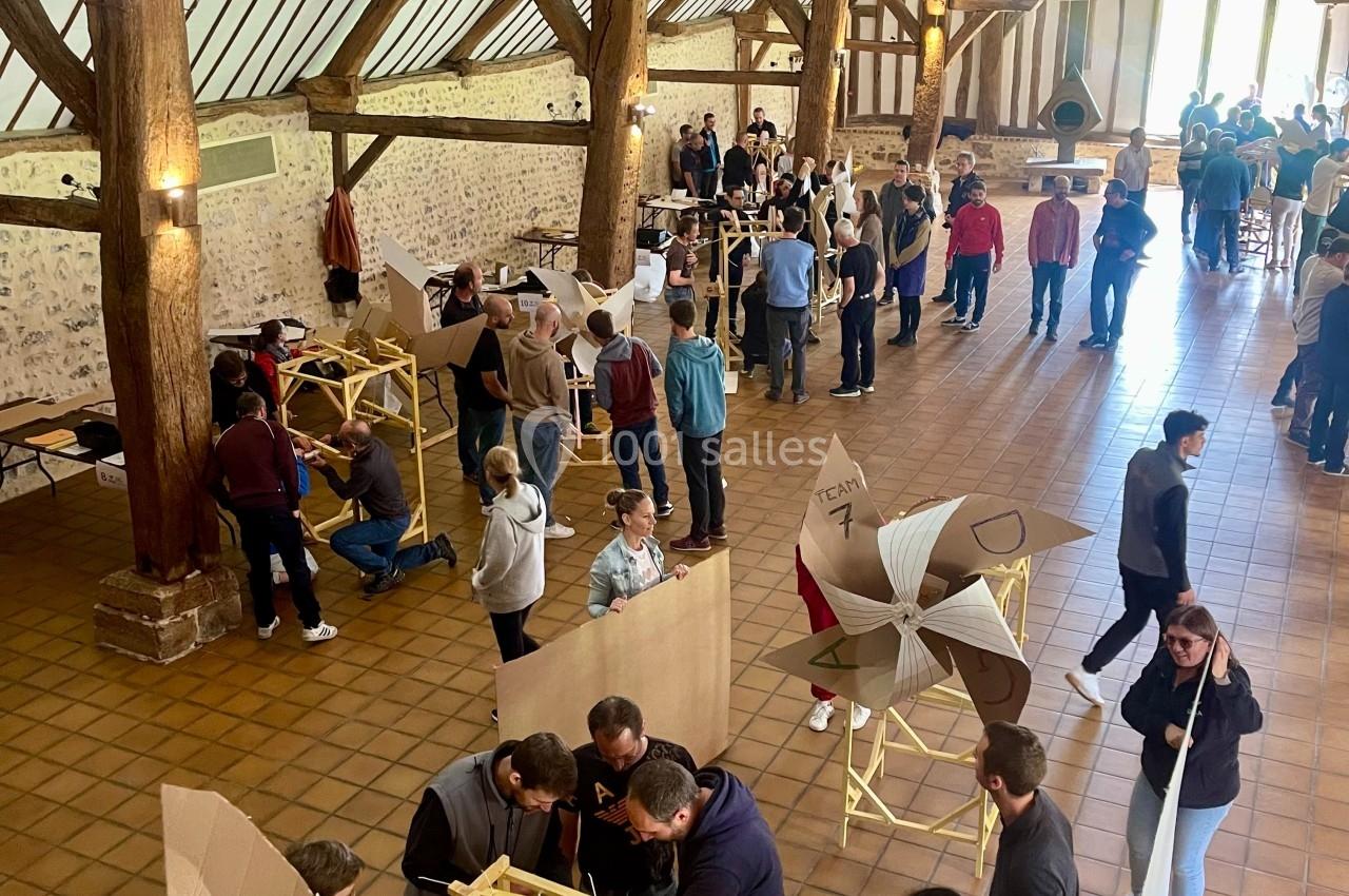 Des personnes participent à un atelier collaboratif dans une grande salle avec charpente en bois et sol en carreaux.