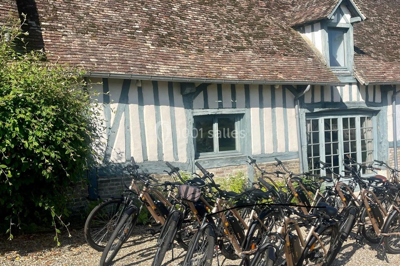 Alignement de vélos électriques devant une maison à colombages avec un toit en tuiles, entourée de végétation.