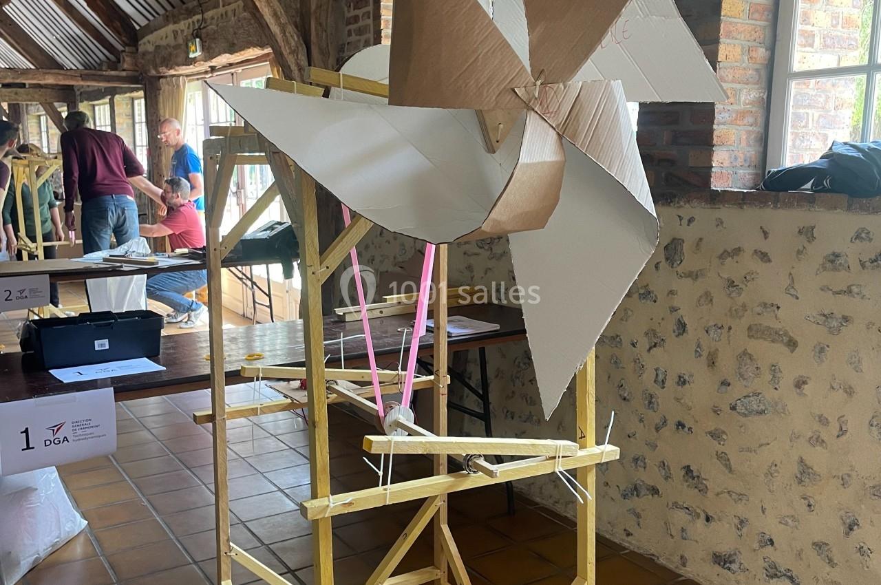 Maquette d'une éolienne en carton et bois exposée dans une salle avec murs en pierre et poutres apparentes.