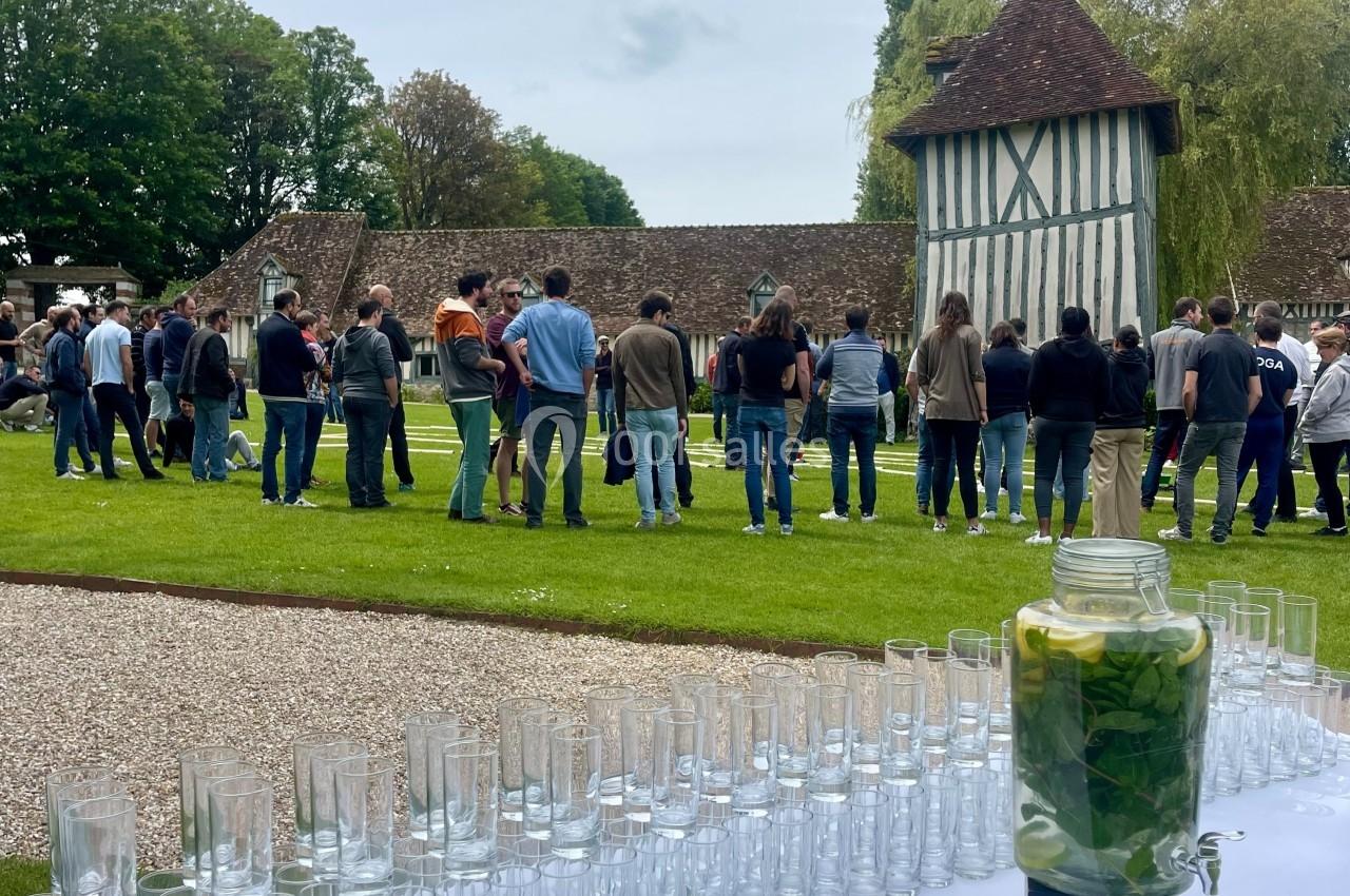 Groupe de personnes rassemblées dans un jardin près d'un bâtiment à colombages, avec une table dressée au premier plan.