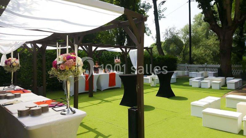 Espace extérieur aménagé avec tonnelle, tables, chaises et décorations florales pour un événement en plein air.