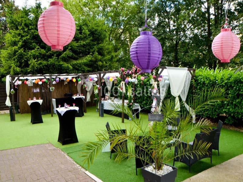 Espace extérieur décoré avec des lanternes colorées, des tables dressées et des plantes, entouré de verdure.