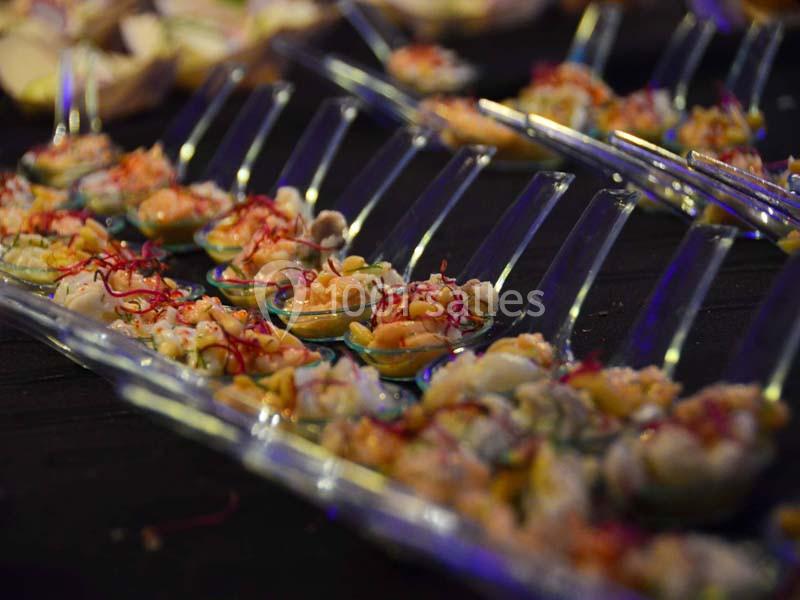 Cuillères transparentes garnies de bouchées colorées à base de fruits de mer, disposées sur une table sombre.