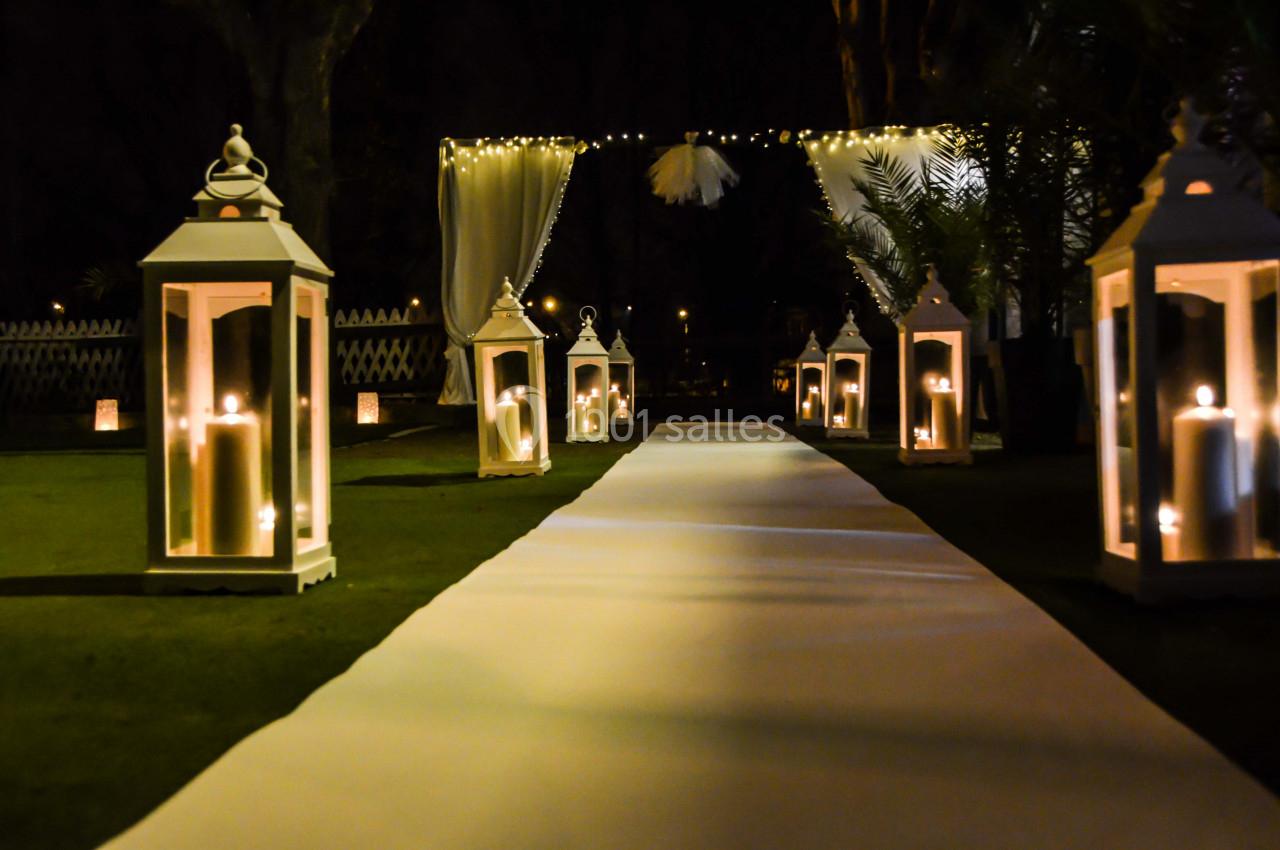Allée extérieure décorée de lanternes éclairées et d'un tapis blanc, menant à une arche illuminée la nuit.