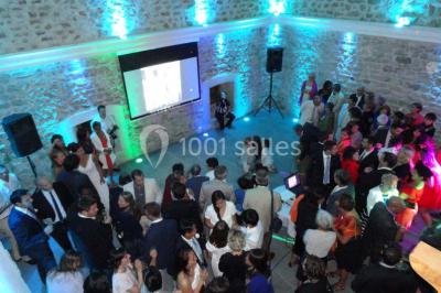 Des personnes en tenue traditionnelle dansent et célèbrent en extérieur, devant des bâtiments en pierre et végétation.