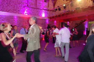 Des personnes en tenue traditionnelle dansent et célèbrent en extérieur, devant des bâtiments en pierre et végétation.