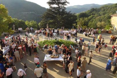 Des personnes en tenue traditionnelle dansent et célèbrent en extérieur, devant des bâtiments en pierre et végétation.
