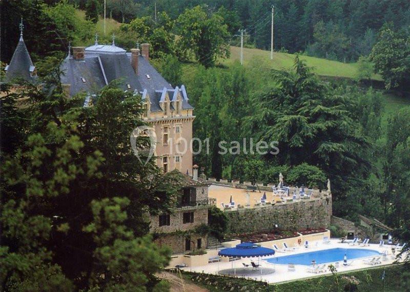 Vue d'un château entouré de verdure avec une piscine et des terrasses aménagées au premier plan.