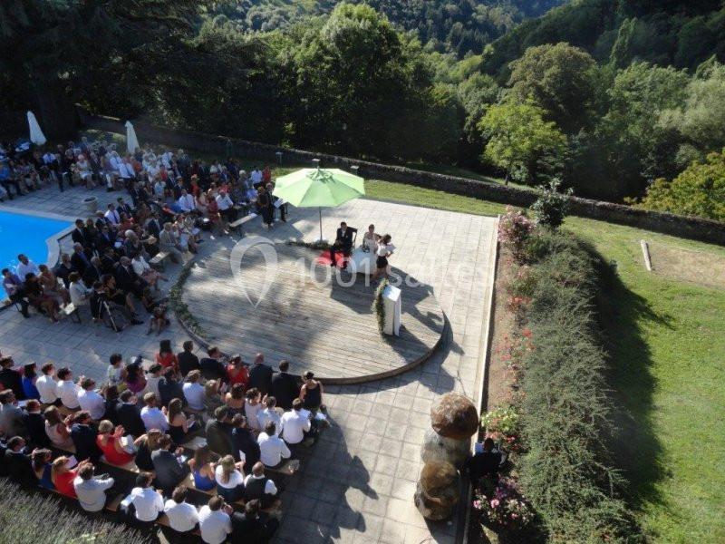 Vue aérienne d'une cérémonie en plein air avec des invités assis autour d'une estrade près d'une piscine et d'un jardin.