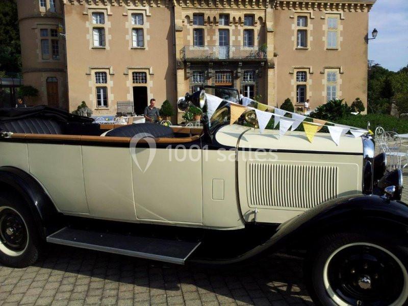 Voiture ancienne décapotable beige stationnée devant un bâtiment historique avec des fanions décoratifs.