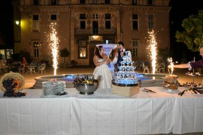 Des personnes en tenue traditionnelle dansent et célèbrent en extérieur, devant des bâtiments en pierre et végétation.