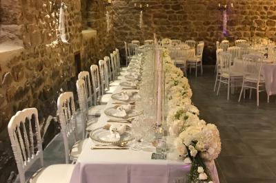 Des personnes en tenue traditionnelle dansent et célèbrent en extérieur, devant des bâtiments en pierre et végétation.