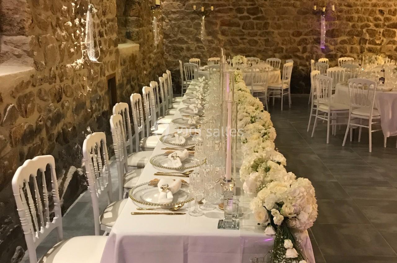 Table de réception élégamment décorée avec des fleurs blanches, dans une salle en pierre avec éclairage chaleureux.