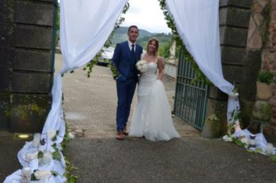 Des personnes en tenue traditionnelle dansent et célèbrent en extérieur, devant des bâtiments en pierre et végétation.