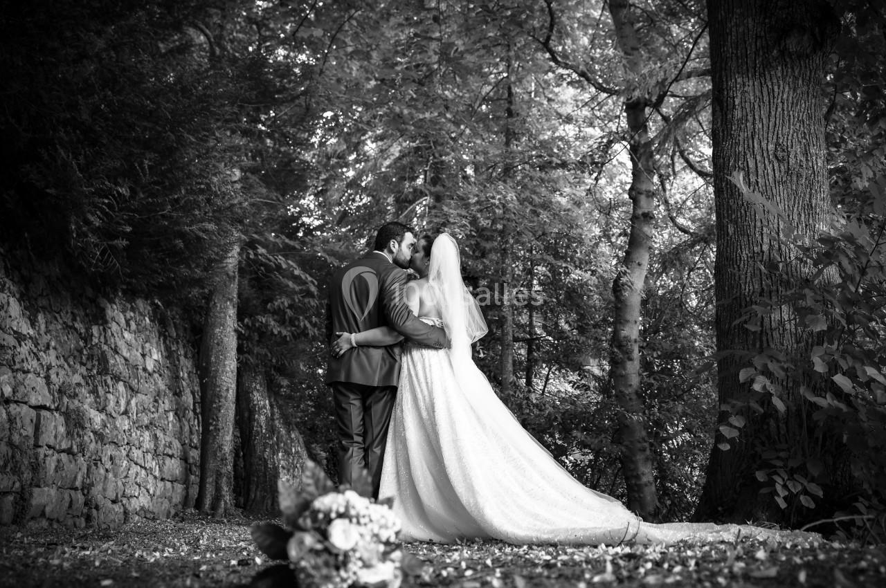 Un couple de mariés de dos, se tenant par la taille dans une forêt, avec un bouquet flou au premier plan.