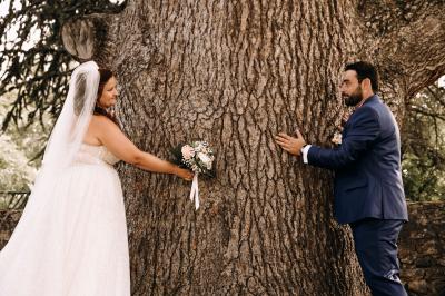 Des personnes en tenue traditionnelle dansent et célèbrent en extérieur, devant des bâtiments en pierre et végétation.