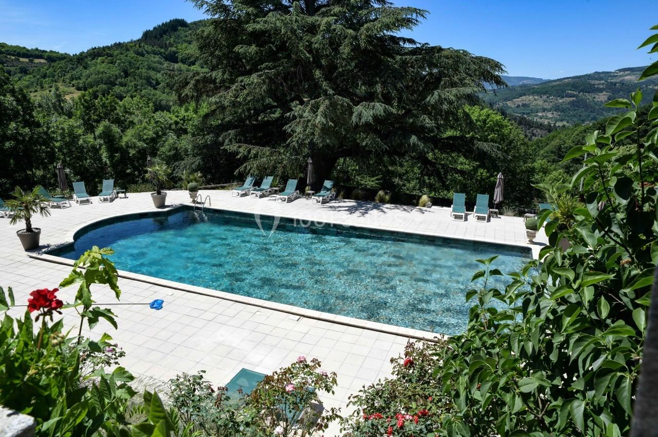 Piscine extérieure entourée de chaises longues, située dans un cadre verdoyant avec vue sur des collines boisées.