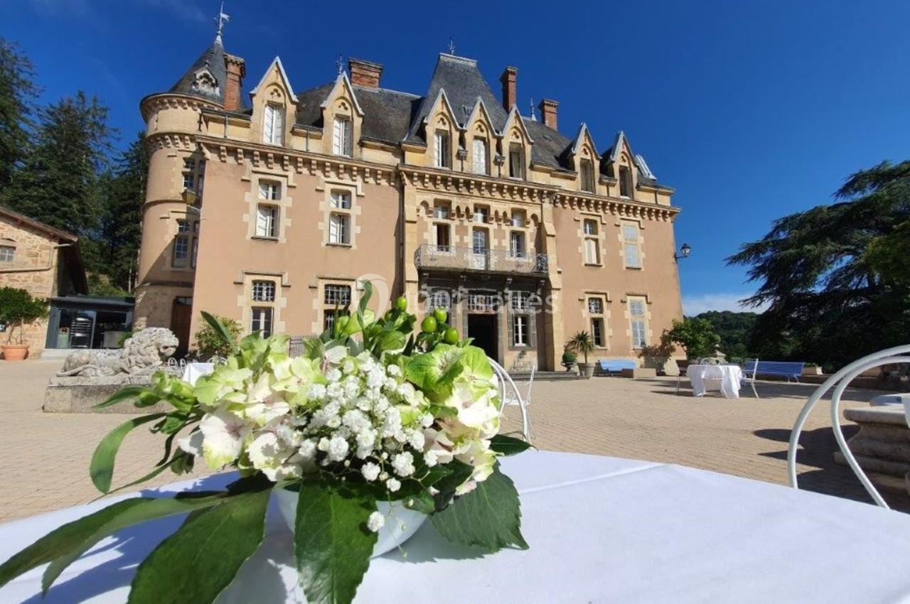 Vue d'un château en pierre avec des fleurs blanches au premier plan sur une table en extérieur.