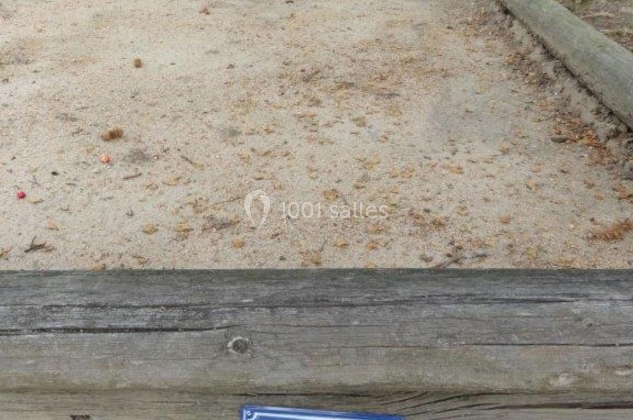 Terrain de pétanque en sable entouré de bordures en bois, avec un panneau indiquant ’Place de la pétanque’.