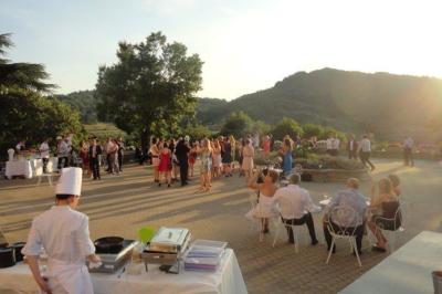 Des personnes en tenue traditionnelle dansent et célèbrent en extérieur, devant des bâtiments en pierre et végétation.