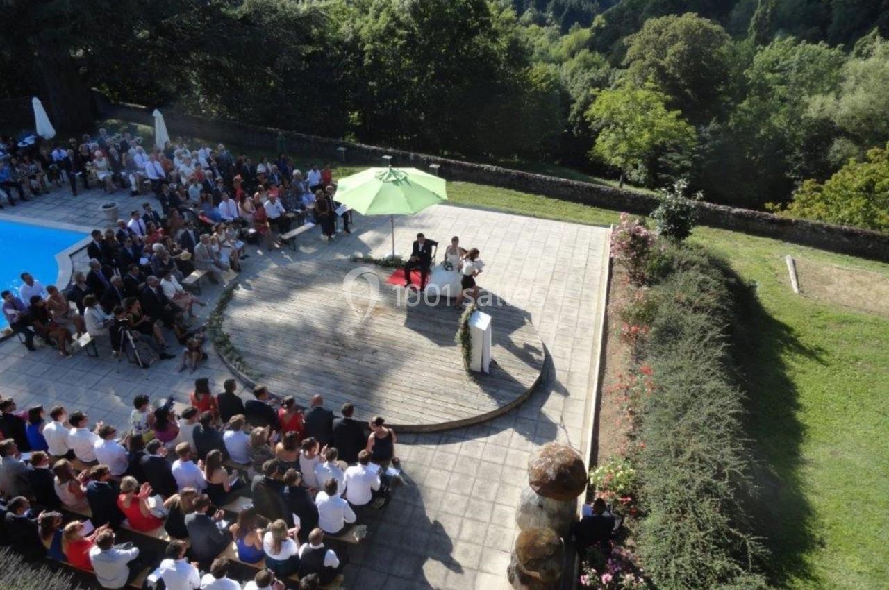 Cérémonie en plein air avec des invités assis autour d'une estrade, entourée de verdure et d'une piscine.