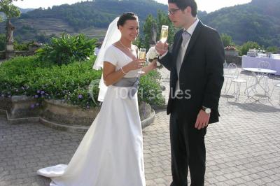 Des personnes en tenue traditionnelle dansent et célèbrent en extérieur, devant des bâtiments en pierre et végétation.