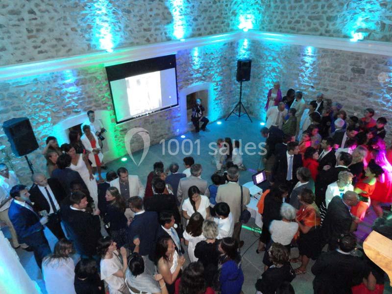 Groupe de personnes rassemblées dans une salle en pierre éclairée par des lumières colorées, avec un écran projetant une…