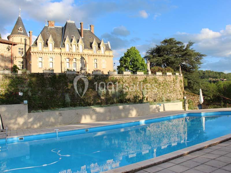 Piscine extérieure devant un château en pierre entouré de verdure sous un ciel bleu.