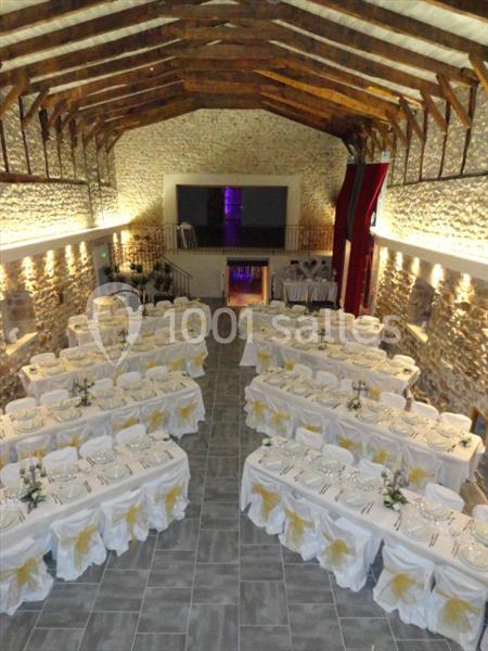 Salle de réception en pierre avec plafond en poutres apparentes, tables dressées pour un événement festif.