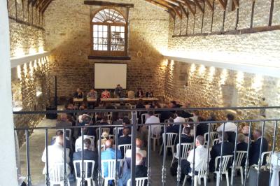 Façade d'un bâtiment ancien avec des arches vitrées, entouré de végétation et d'un escalier sur la gauche.