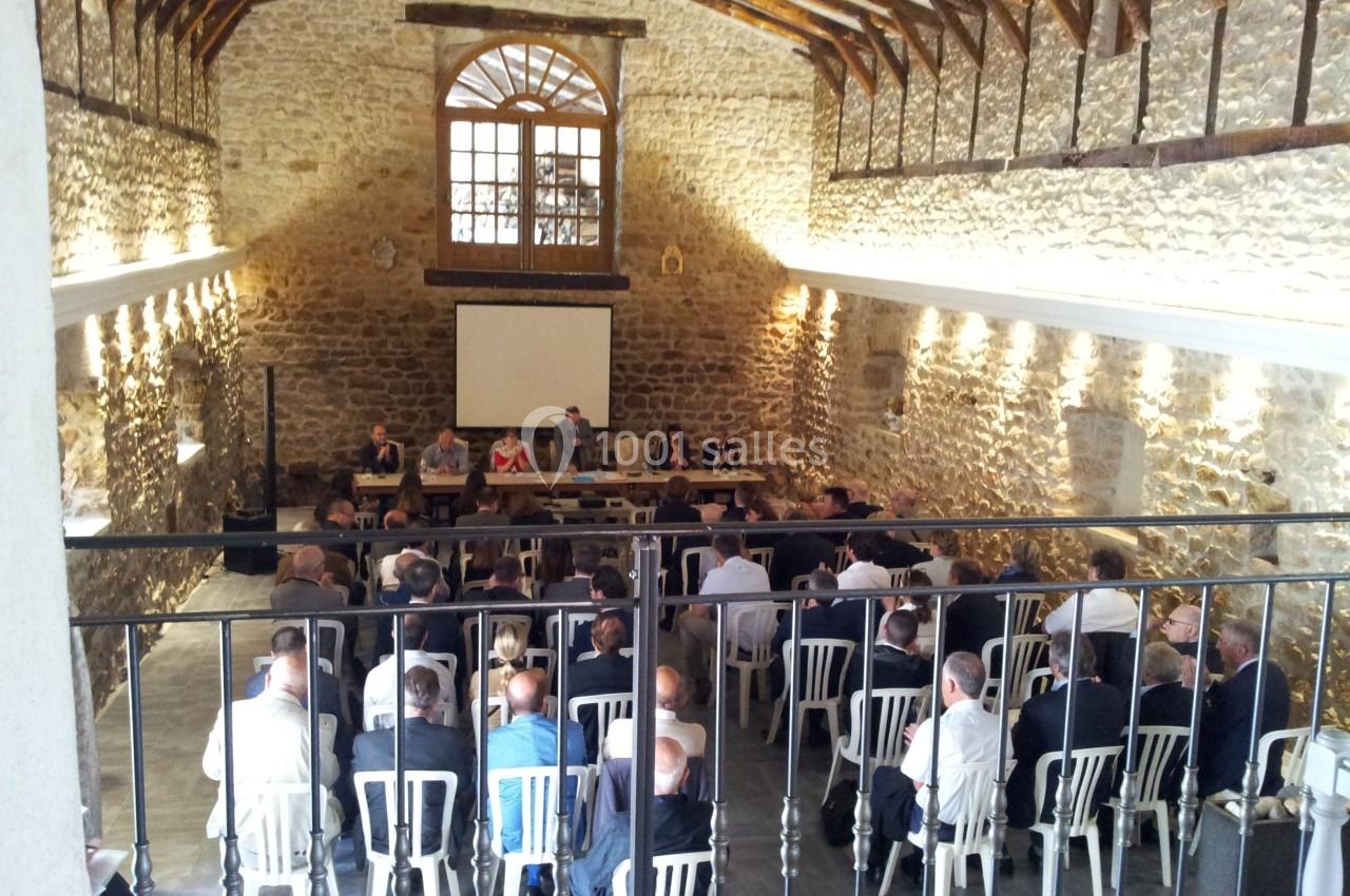 Salle en pierre avec plafond en poutres apparentes, réunion de personnes assises face à un panel et un écran de projection.