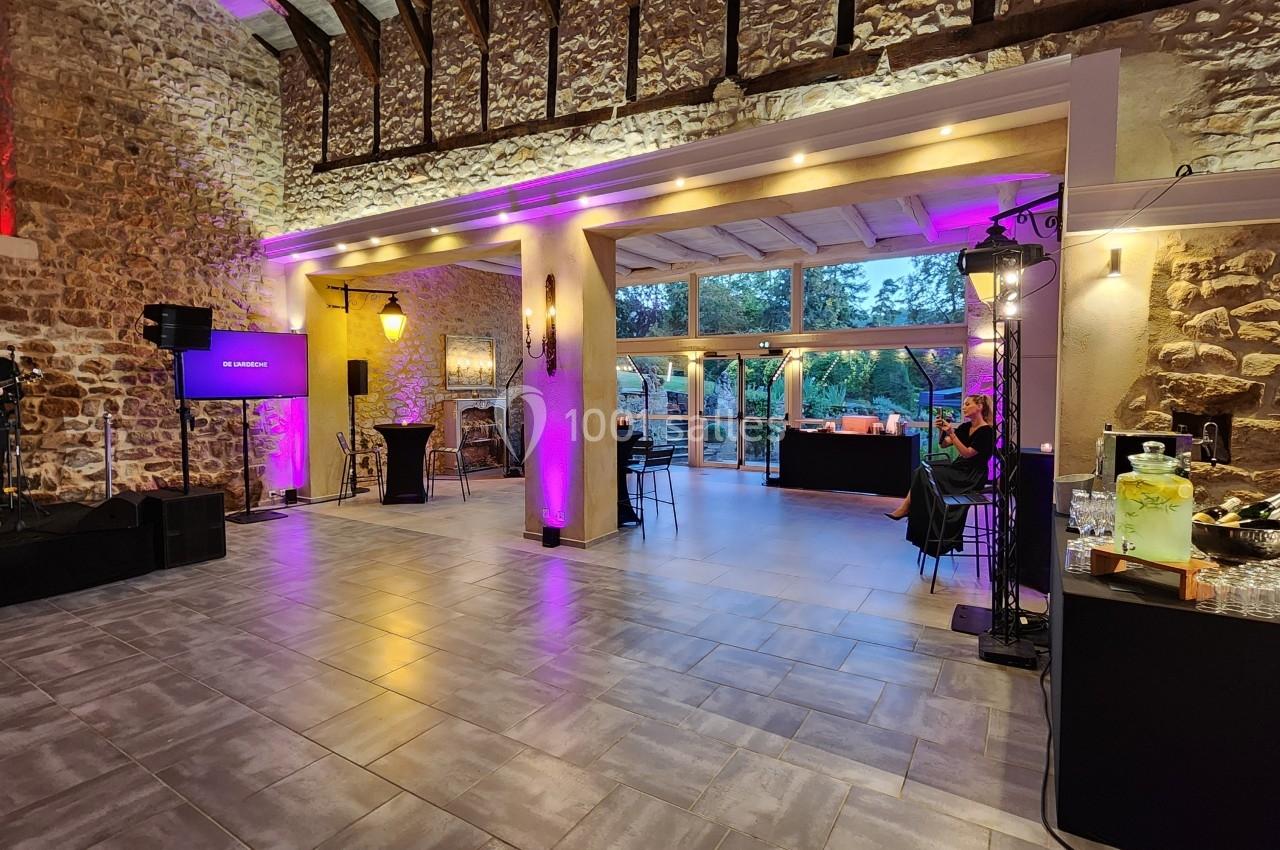 Salle en pierre avec éclairage violet, espace aménagé pour un événement, bar et musicien sur scène à gauche.