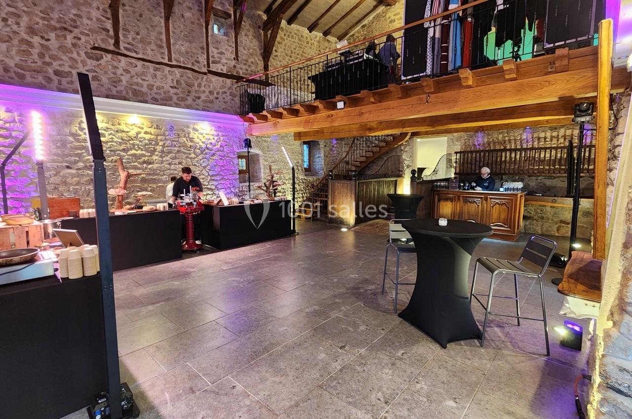 Salle en pierre avec éclairage coloré, tables hautes et espace buffet, ambiance événementielle chaleureuse.