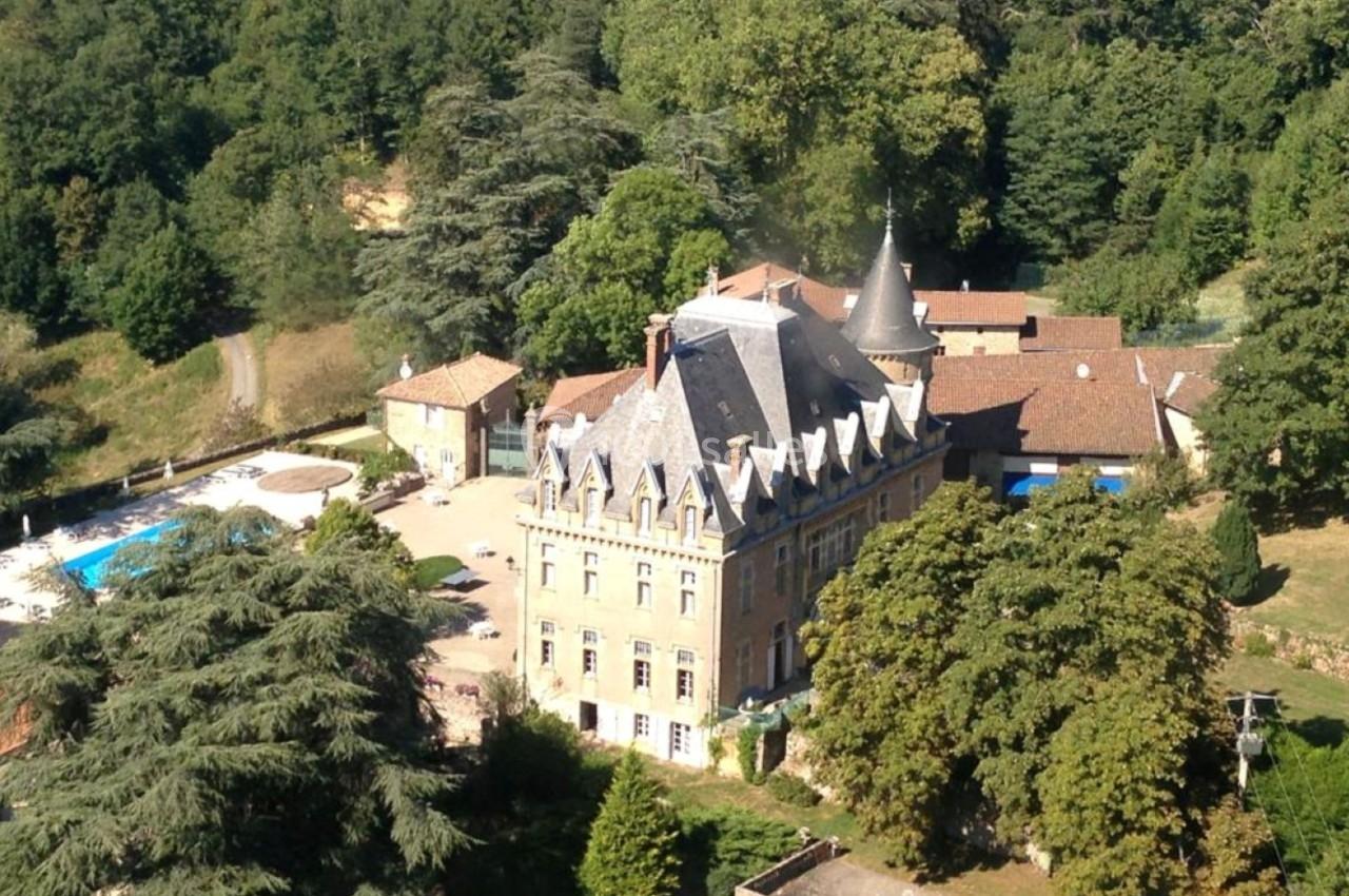 Vue aérienne d'un château entouré de verdure, avec une piscine et des bâtiments annexes à proximité.