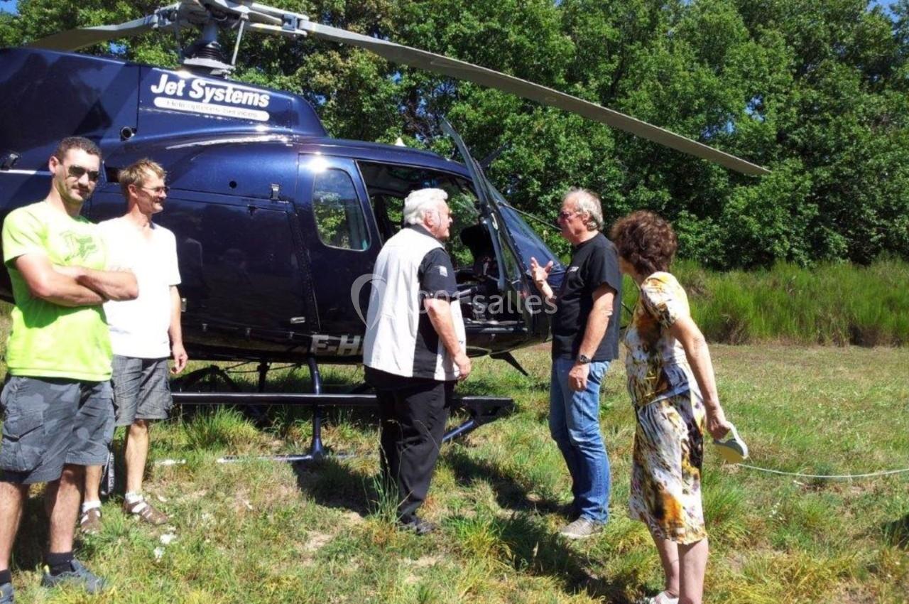 Un groupe de personnes discute près d'un hélicoptère noir stationné sur une zone herbeuse.