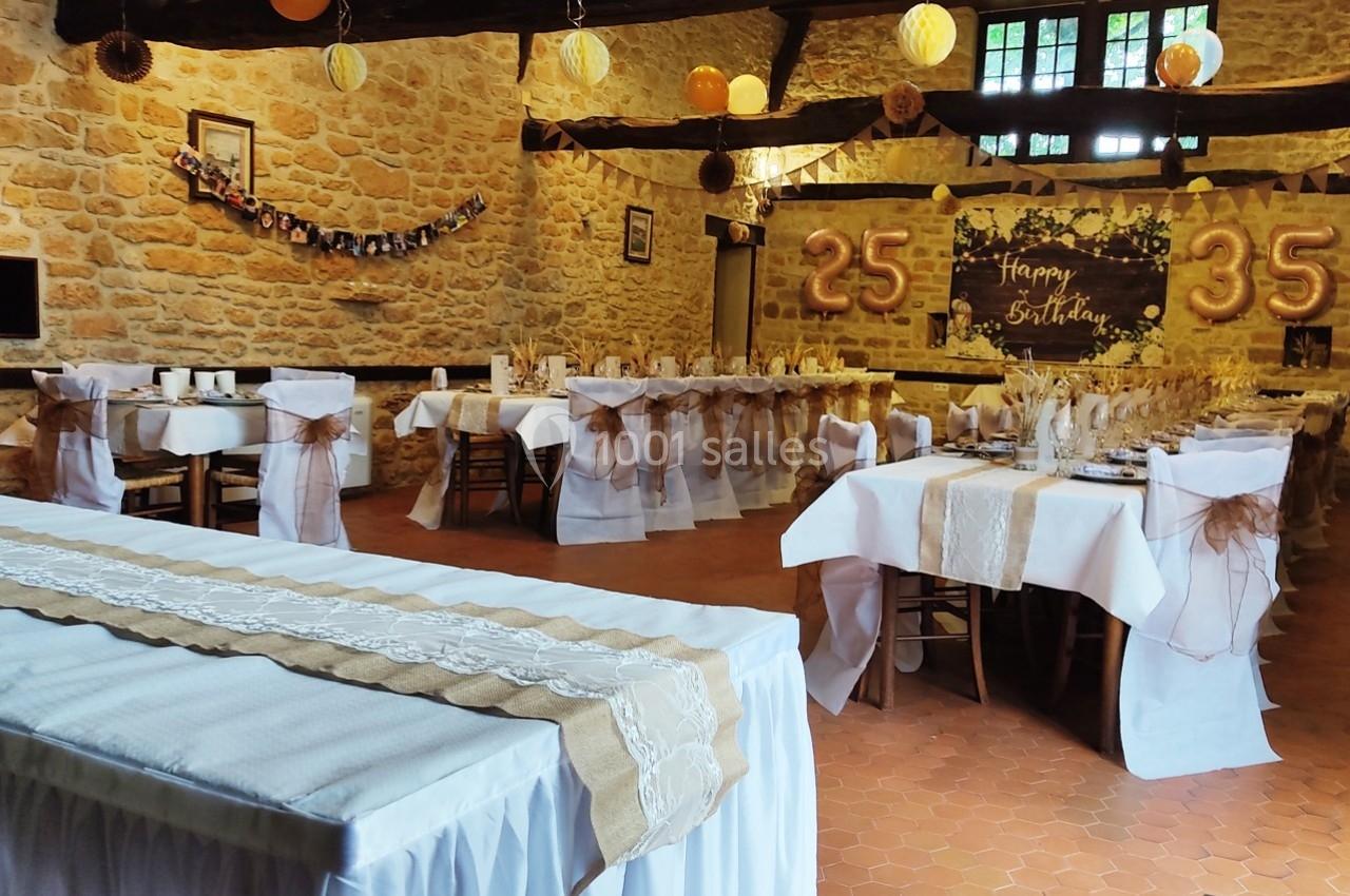 Salle décorée pour une fête d'anniversaire avec tables dressées, guirlandes et chiffres ’25’ et ’35’ en arrière-plan.