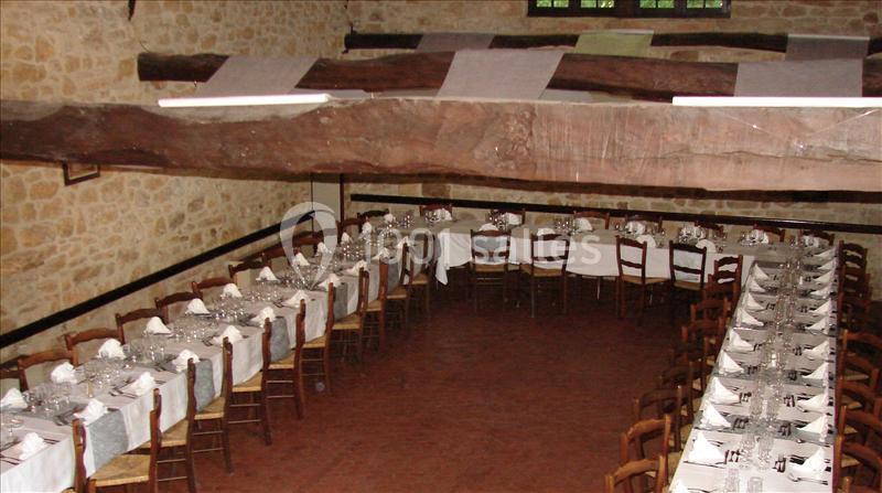 Deux longues tables dressées avec nappes blanches et vaisselle, alignées dans une salle rustique aux murs en pierre et…