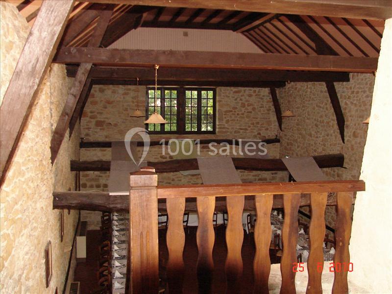 Vue intérieure d'une pièce avec des murs en pierre, une charpente en bois apparente et une rambarde en premier plan.
