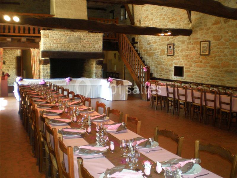 Salle de réception rustique avec de longues tables dressées, nappes roses et poutres apparentes en bois.