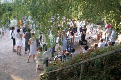 Groupe de personnes rassemblées en extérieur sous des arbres, discutant près de tables et de chaises.