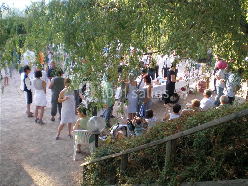 Groupe de personnes rassemblées en extérieur sous des arbres, discutant près de tables et de chaises.
