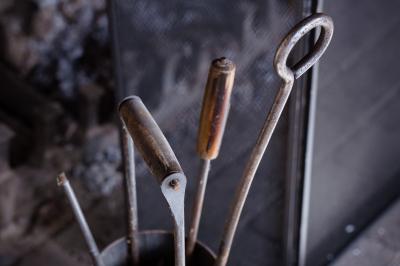 Outils en métal pour cheminée rangés dans un support cylindrique devant un pare-feu en métal.